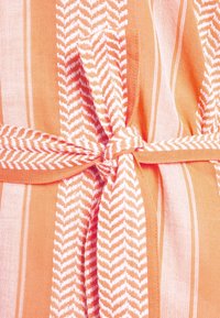 Oranžovo-bíle pruhovaná látka s vzorem rybí kosti, obsahující detail zavázaného pásku, hladkou texturu a lehký vzhled.