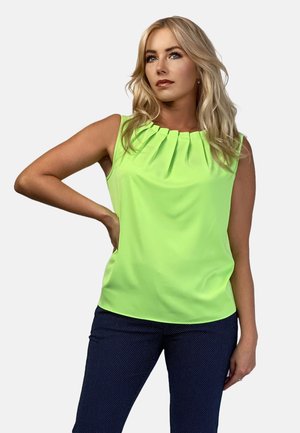 Neon zielona bluzka bez rękawów z plisowanym dekoltem, lekkiego materiału, gładkiej tekstury, w zestawieniu z ciemnymi wzorzystymi spodniami.