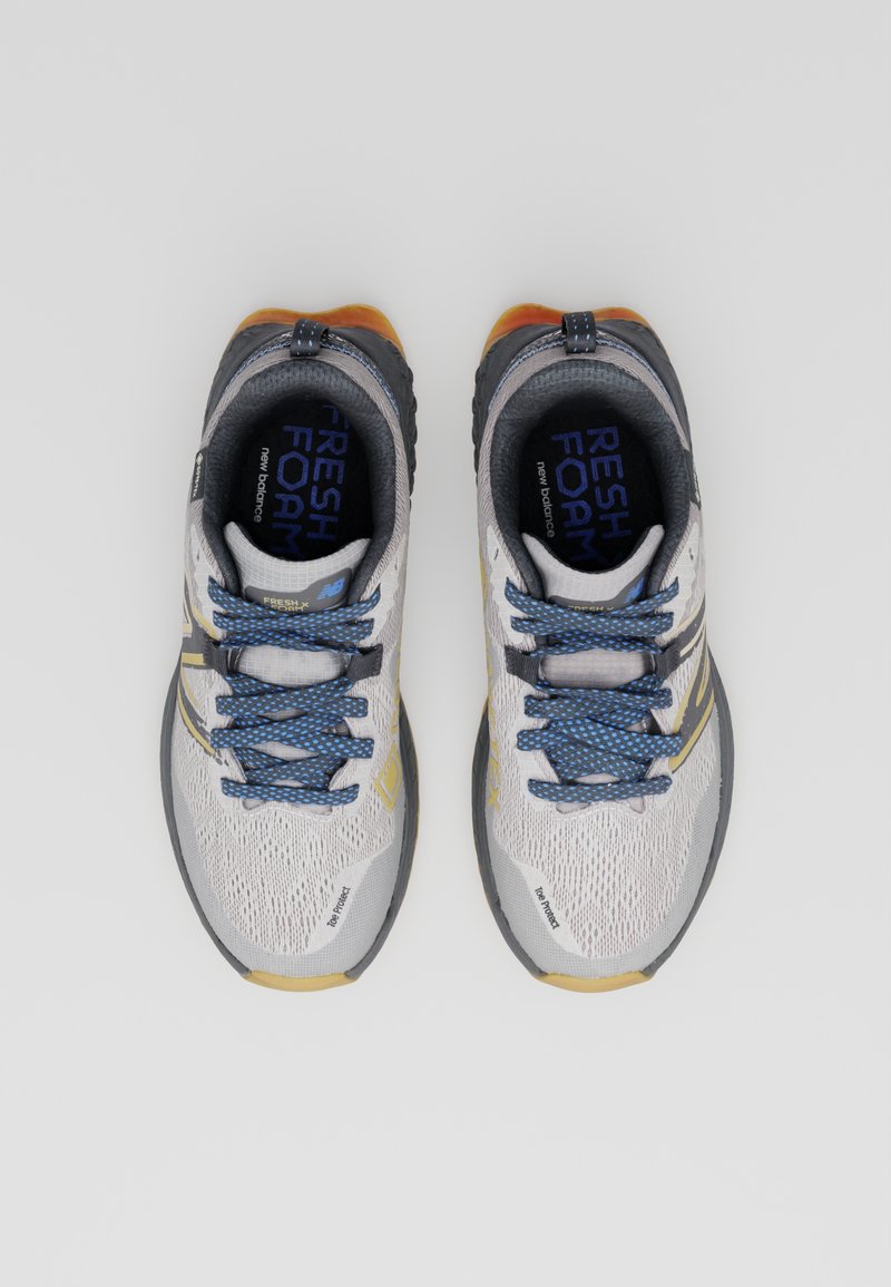Zapatillas de running color gris claro con parte superior de malla, cordones azules, detalles amarillos y suela negra duradera. Presentan la marca "Fresh Foam".