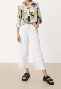 Värikäs, kuvioitu keltainen, musta ja vihreä nappipaita; yhdistetty valkoisiin, korkeavyötäröisiin leveälahkeisiin farkkuihin ja mustiin korokepohjasandaaleihin.