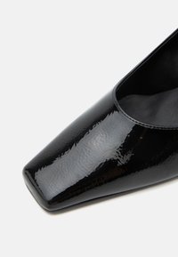Chaussure en cuir verni noir avec un bout carré et une tige lisse texturée, vue de face côté droit.