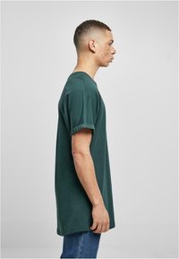 Camiseta de algodón de color verde oscuro con mangas cortas enrolladas, corte relajado y cuello redondo, combinada con jeans de denim azul.