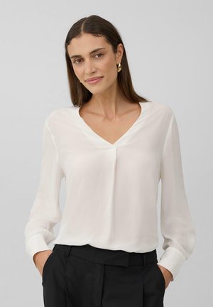 Witte blouse met lange mouwen en V-hals, zachte textuur en een gedrapeerd ontwerp. Gecombineerd met zwarte broek.
