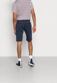 Námořnické šortky vyrobené z bavlny, s kapsou na zadní straně. V kombinaci s pruhovaným vínovým a bílým tričkem a modrými teniskami s vyšším střihem.