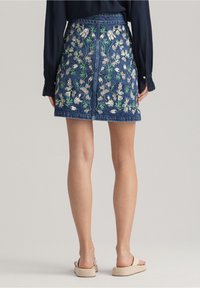 Falda de denim con bordado floral en verde y blanco, con un corte ajustado y una parte trasera sin costuras. Llevada con sandalias de color neutro.