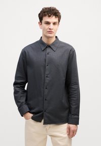 Camicia a maniche lunghe di colore grigio scuro con colletto e una trama sottile. Presenta bottoni neri e un piccolo logo sul petto.