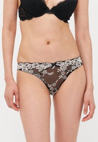Black lace thong with floral lace waistband, sheer mesh body, and scalloped edges. Detailed floral pattern adds texture and contrast.