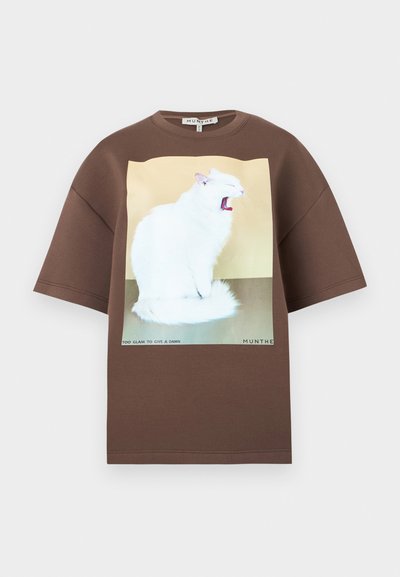 Καφέ κοντομάνικη μπλούζα με γραφικό λευκής γάτας που χασμουριέται σε μπεζ και γκρι φόντο, κείμενο «Too glam to give a damn.»