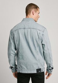 Lichtblauwe denimjack met een klassieke kraag, zijkanten en knoopmanchetten. Bevat een zwart label aan de zoom. Zware textuur.