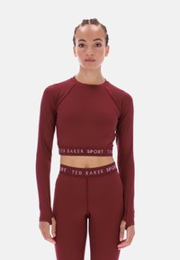 Bordó sportos crop top hosszú ujjakkal és testhez simuló szabással. Kontrasztos derékrésszel, rajta a "TED BAKER SPORT" logóval.