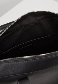 Sac en cuir noir ouvert montrant une doublure en tissu lisse et une poche intérieure avec des coutures visibles et une fermeture éclair argentée.