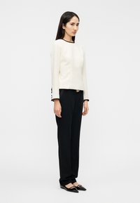 Λευκό μακρυμάνικο τοπ με μαύρο περίγραμμα, συνδυασμένο με μαύρο παντελόνι και μυτερές μπαλαρίνες. Το τοπ έχει πλευρικά κουμπιά και δομημένη εφαρμογή.