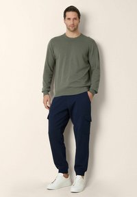 Zielony sweter z dzianiny z okrągłym dekoltem, zestawiony z granatowymi spodniami cargo z bocznymi kieszeniami oraz białymi sneakersami. Prosty, casualowy design.