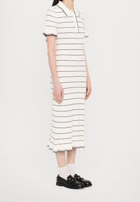 Robe tricotée blanche avec de fines rayures bleues, à manches courtes et un col ; assortie à des chaussures noires à enfiler et des chaussettes blanches.