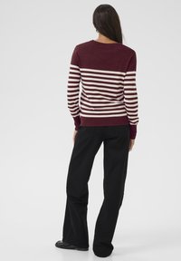 Pull rayé bourgogne et crème avec un col ras du cou, des manches longues et des poignets côtelés, accompagné d'un pantalon large noir.