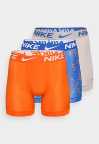 Tri para kratkih Nike bokseric: oranžne, modre z vzorcem in bež. Imajo elastične pasove z jasno prikazanim logotipom Nike.