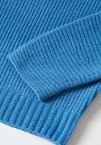 Ribbeliger blauer Wollstoff mit einer weichen Textur, der einen gefalteten Abschnitt zeigt, der vertikale Linien und gleichmäßige Nähte entlang der Ränder aufweist.