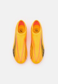 Scarpe da calcio gialle brillanti con parte superiore testurizzata, caratterizzate da accenti in gradiente nero e rosa e un design slip-on per una vestibilità aderente.