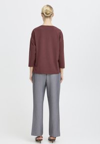 Burgunderrotes langärmliges Strickoberteil kombiniert mit grauen weiten Hosen. Saubere Silhouette, glatte Textur und weicher Stoff sind von hinten sichtbar.