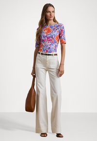 Haut ajusté fleuri avec des tons bleus, oranges et roses ; pantalon large taille haute blanc avec des boutons sur le devant ; sac en cuir marron.