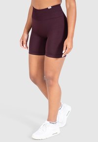 Shorts de ciclismo de talle alto en burdeos, hechos de una tela elástica, con una textura suave y un diseño ajustado, combinados con zapatillas blancas.