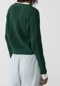 Green knitted sweater with a ribbed hem and cuffs, slightly cropped, paired with light gray sweatpants featuring a relaxed fit.