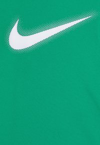 Zielona tkanina sportowa o teksturowanej powierzchni z dużym białym logo Nike w postaci charakterystycznego znaku, stworzonego za pomocą punktowego gradientu.