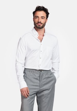 Weißes Langarmhemd mit Button-Down-Kragen und Brusttasche. Kombiniert mit grauen Hosen mit elastischem Bund. Glatte Stofftextur.