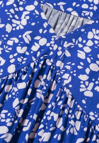 Blaues Kleid mit einem weißen abstrakten Muster, einem gefalteten Oberteil und einem V-Ausschnitt. Hergestellt aus einem weichen, strukturierten Stoff.