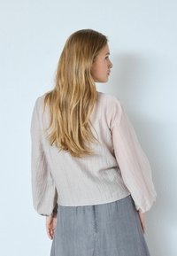 Lyserød, tekstureret bluse med puffede ærmer, kombineret med en grå nederdel; afslappet, flydende design egnet til forskellige lejligheder.