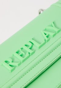 Borsa in pelle sintetica verde con lettering in rilievo "REPLAY", texture liscia e dettagli di cucitura visibili lungo i bordi.
