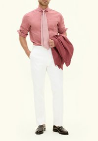 Ljust rosa skjorta med knappar och ett matchande mönstrat slips, vita byxor och svarta loafers. Figuren håller en mörk rosa jacka.