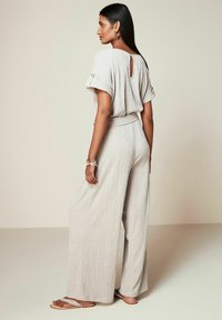 Jumpsuit grigio chiaro con una finitura texturizzata, gambe ampie, maniche corte, un'apertura a chiave sulla schiena e una cintura abbinata in vita. Design semplice e fluido.