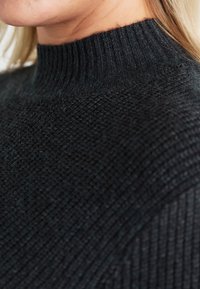 Black knitted sweater with a high ribbed neckline, featuring a textured pattern and soft, fuzzy material. Close-up detail shows the weave.