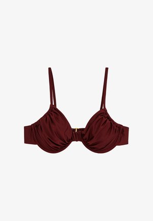 Burgundia värvi traadiga rinnahoidja kortsuliste tissidega, õhukeste kahekordsete õlapaeltega ja esiküljel kuldse konksuga kinnitusega, valgel taustal.