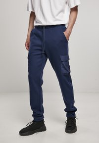 Marineblauwe joggers met een koord in de taille, een cargozak op het linkerbeen en geribbelde boorden. Gecombineerd met zwarte sportschoenen.