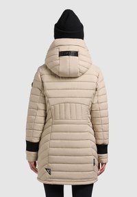 Beige Pufferjacke mit Kapuze, gestepptem Design, schwarzen Strickbündchen und einem gummierten Logodetail auf dem Rücken. Verstärkte Nähte sichtbar.