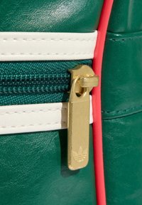 Zielona torba z eko skóry z złotym zamkiem błyskawicznym, białymi i różowymi akcentami oraz teksturowanymi detalami powierzchni z logo na suwaku.
