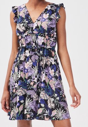 Robe noire sans manches avec imprimé floral tropical violet, rose et blanc, encolure en V à volants et taille élastique portée par une personne debout.