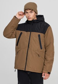 Brązowa i czarna puchowa kurtka z kapturem, z przednimi zamekami i bocznymi kieszeniami, charakteryzująca się gładką teksturą i regulowanymi sznurkami u dołu.