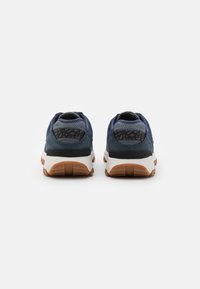 Kék és szürke sneaker, texturált felsőrésszel, párnázott nyakkal és gumitalppal. Kontrasztos fekete részletekkel és gumi talppal rendelkezik.
