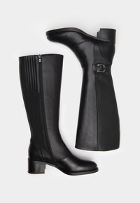 Bottes noires en cuir montantes avec une finition lisse, dotées d'une fermeture éclair latérale et de détails décoratifs en métal sur la tige. Semelle en caoutchouc et talon large.