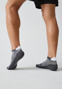 Graue Sneakersocken mit weißen Bündchen, die ein strukturiertes Mesh-Design und eine durchgehende Ferse aufweisen. Leichtes Material für Atmungsaktivität und Komfort.