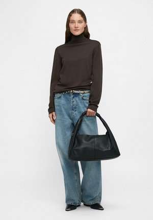 Czarna skórzana torebka o zaokrąglonym kształcie, trzymana przez osobę w brązowym golfie i jasnoniebieskich szerokich spodniach. Gładka faktura.