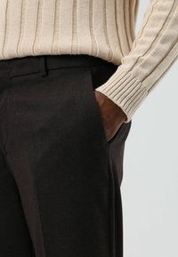 Beige geribbelde gebreide trui gecombineerd met donkerbruine broek met zijzak en een gladde textuur. Accentueert met een omslagmouw.