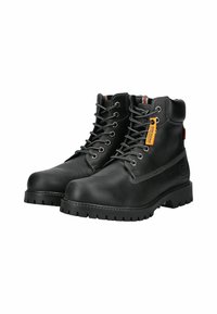 Botas de trabajo de cuero negro con cuello acolchado, suela de goma gruesa, costuras detalladas y una etiqueta adjunta con el nombre de la marca y su logotipo.
