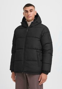 Giacca a vento nera con cappuccio, dotata di zip frontale, polsini elasticizzati e tasche laterali. Texture liscia e design trapuntato.
