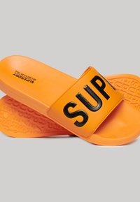 Oranje rubberen slide sandalen met een brede zwarte band waarop het woord "SUPER" staat. Textured voetbed met reliëfpatronen en logo-details.