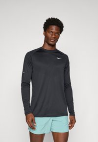 Sort langærmet sportstrøje med et tekstureret mønster på brystet, der har et fremtrædende hvidt Nike-logo på venstre side.