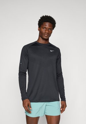 Sort langærmet sportstrøje med et tekstureret mønster på brystet, der har et fremtrædende hvidt Nike-logo på venstre side.